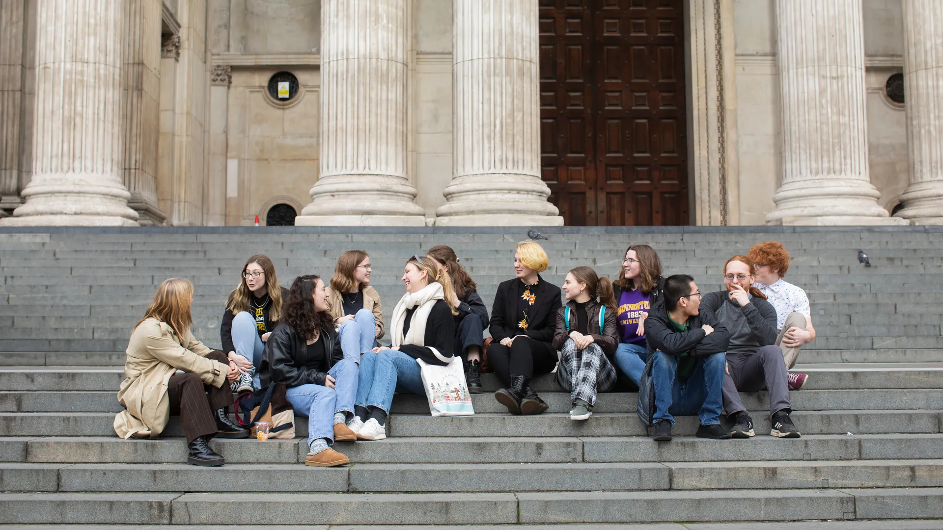 ���Ͽ� honors student sitting on the steps in front of historic European building.