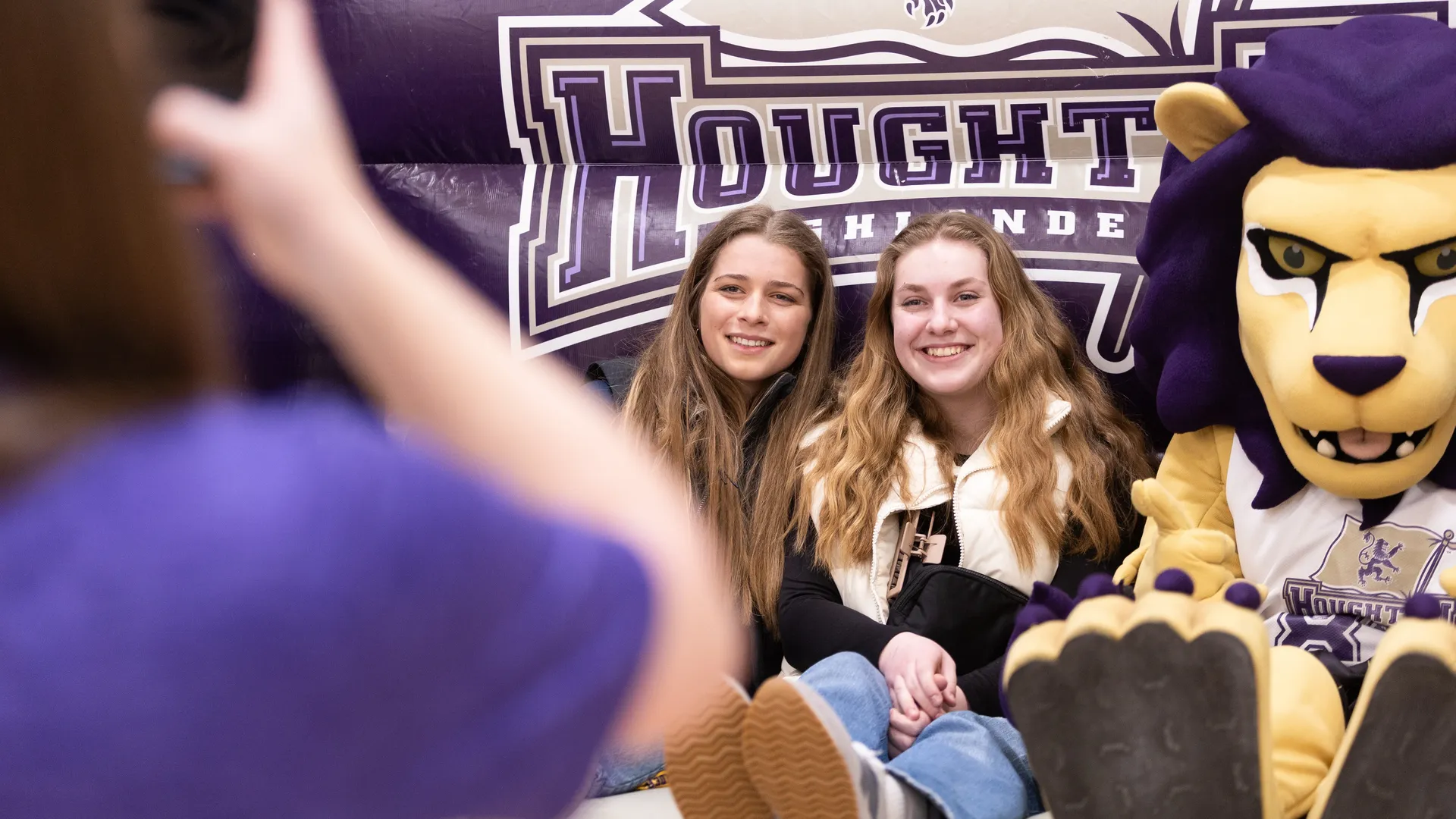 Two Houghton accepted students sitting on giant inflatable chair with Luckey the lion mascot.